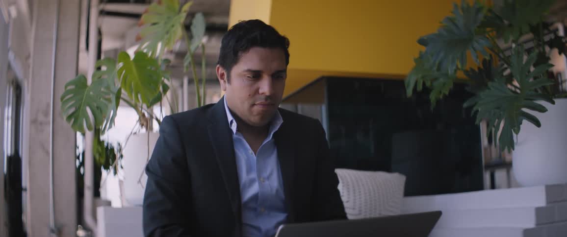 A man uses a laptop while he sits on furniture inside of a building