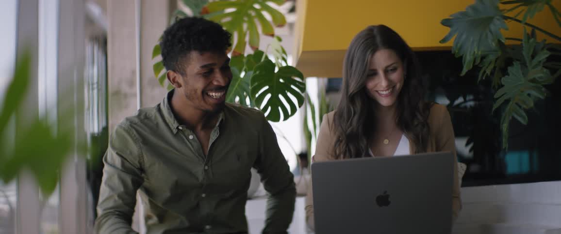 A man and woman laugh while looking at a laptop