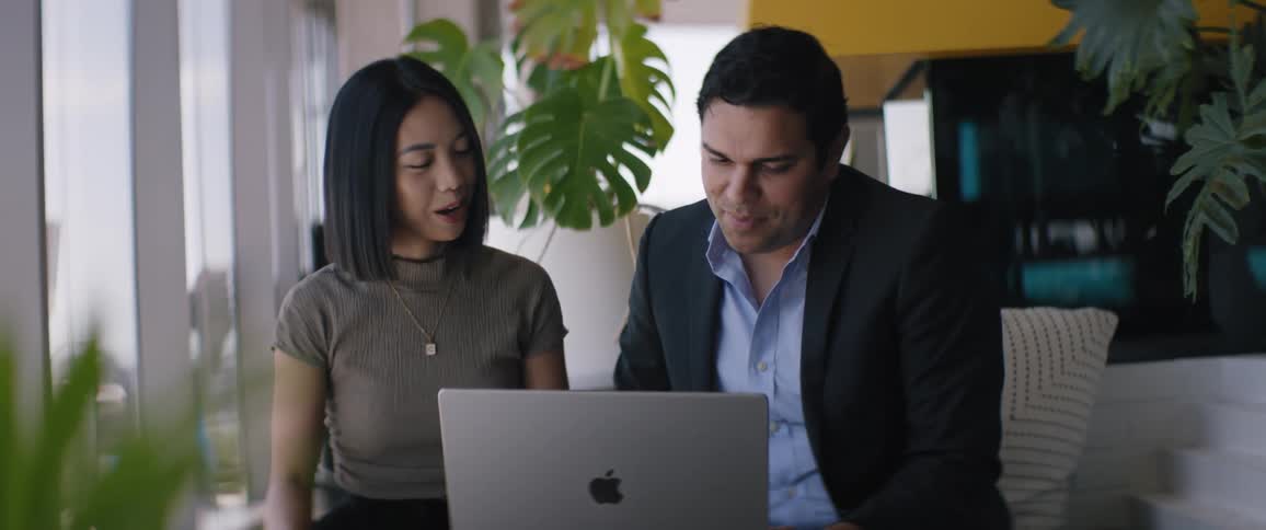 Man and woman sitting side by side and talking smilingly while a laptop is open in front of them