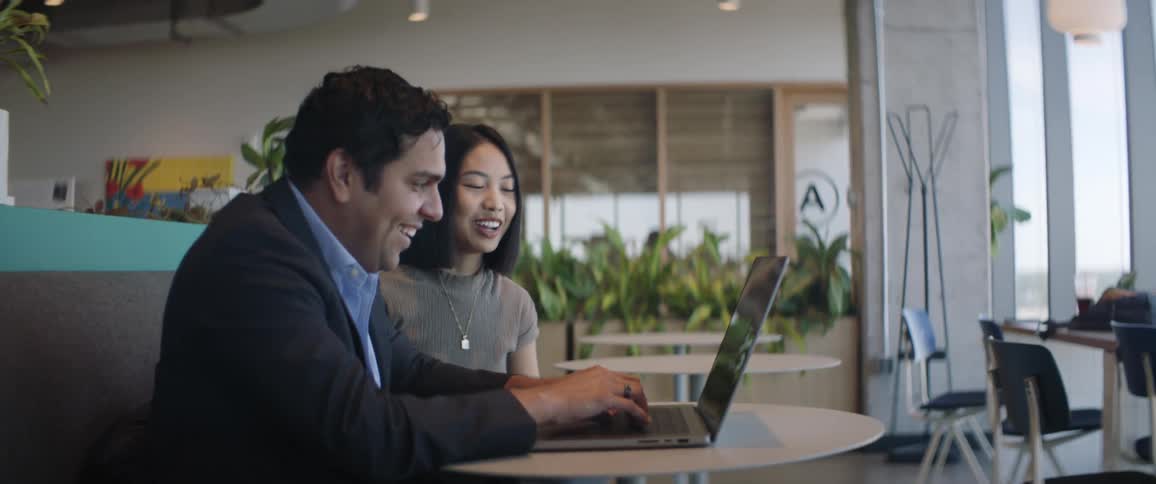 A man and a woman are talking and smiling while the man keys on the laptop