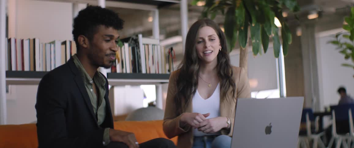 Woman sitting next to a man talking in a work environment and using a laptop