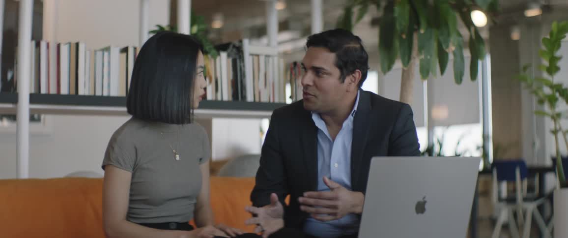A man and a woman greet each other by shaking hands and then sit on a sofa and start talking