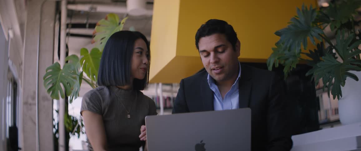 A man and a woman are sitting looking at a laptop and they are happy while talking