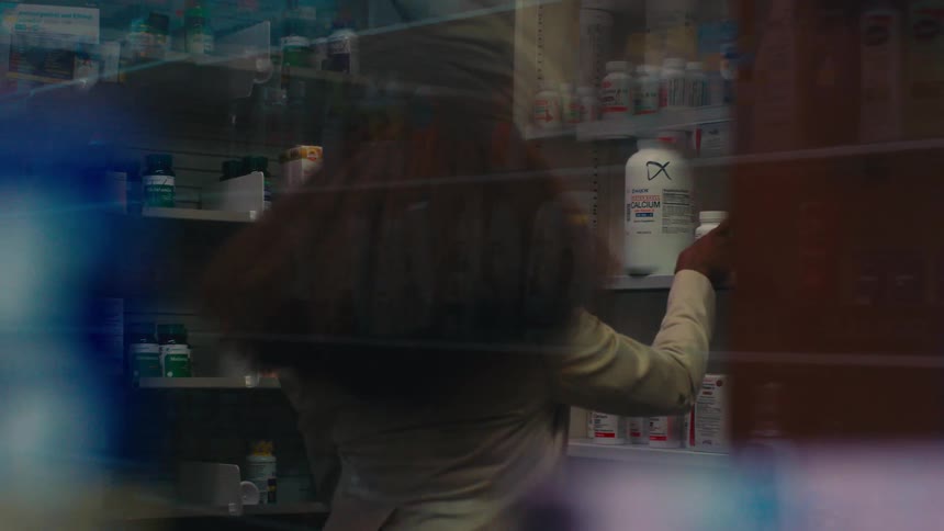 A black woman chooses a product in a pharmacy and walks to a counter