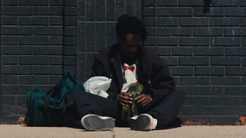A man is lying on a sidewalk and there are several cars passing in front of him