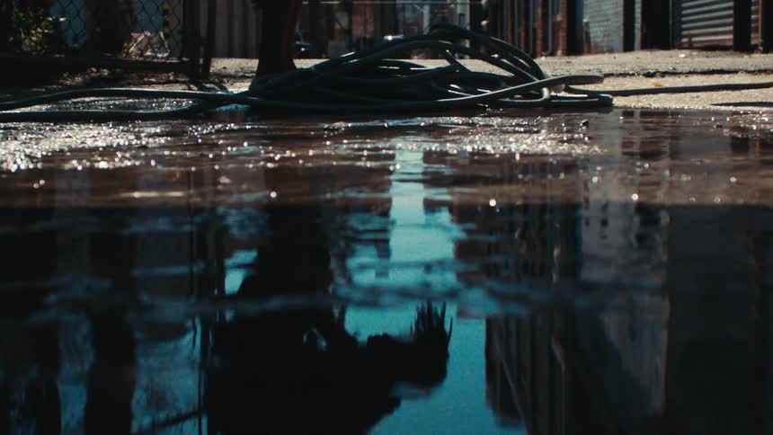 Puddle reflects man wiping his legs off with water from a hose