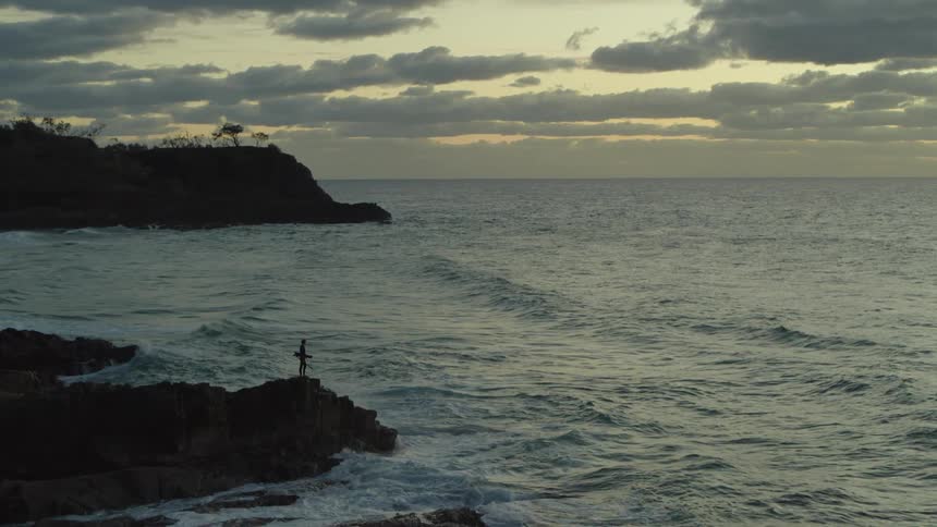 Aerial panorama of a person on a rock peak in front of a beach as the day dawns