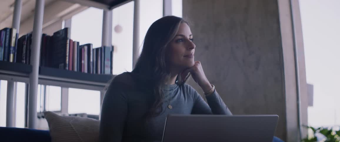 Portrait of a woman in a work environment sitting using her laptop and placing one of her hands on her chin