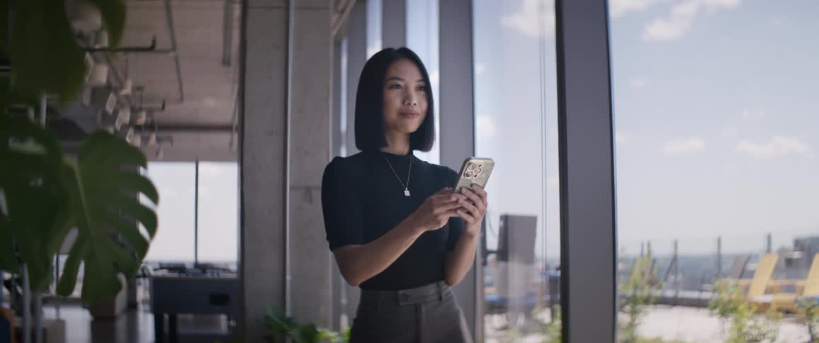 Woman standing near a window holding and looking at a smartphone