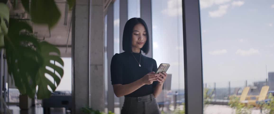 A young woman standing next to a glass window and using her cell phone