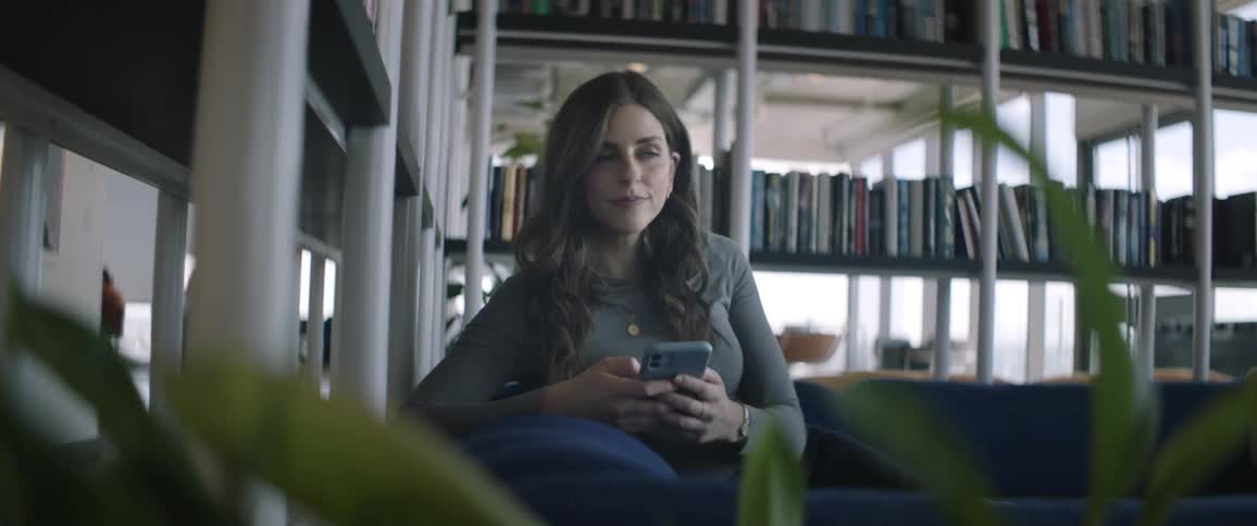 Woman sitting in an armchair using her smartphone and bookshelves around her