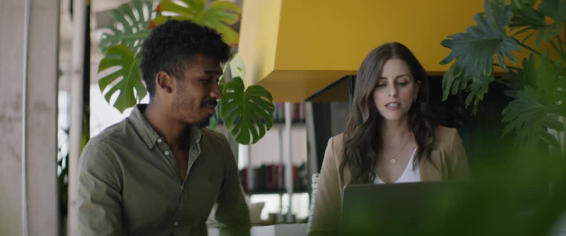 Man and woman sitting in front of a laptop talking in a work environment