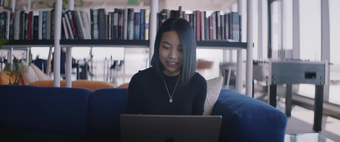 Woman sitting on a blue sofa using a laptop