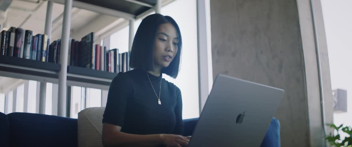 A young asian woman in a library talks via a laptop