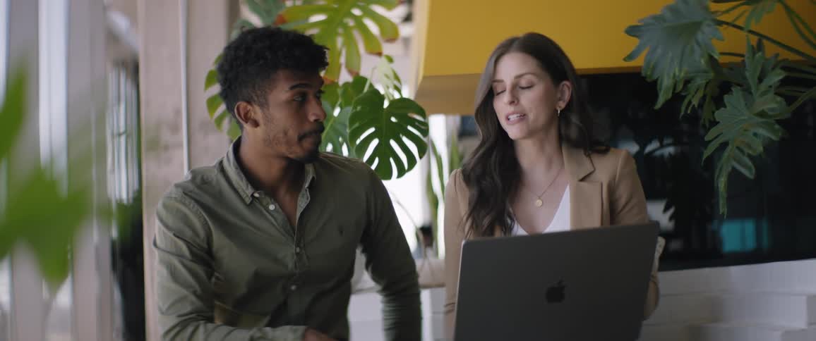 Man and woman sitting in an office space talking and using a laptop