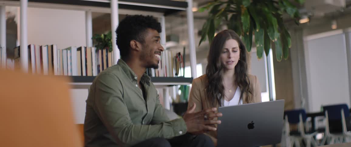 A man and a woman are talking and the woman has a laptop on her legs