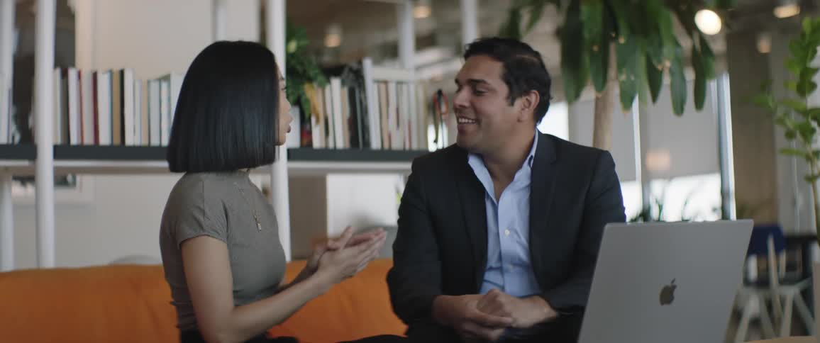 Man and woman greeting each other and then sitting in front of a laptop in an office