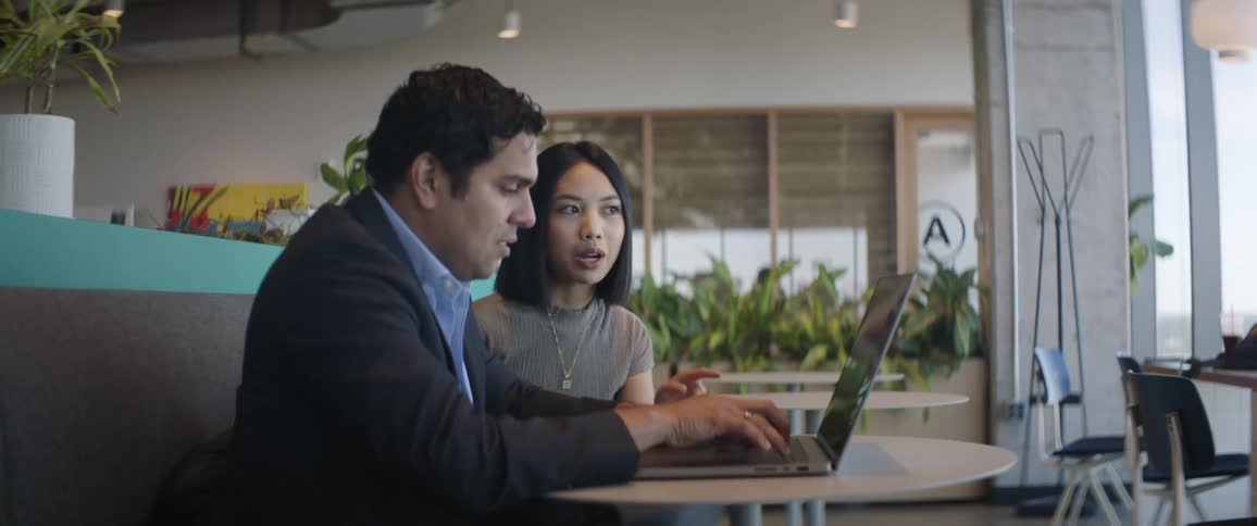 Woman and man sitting at a table typing on a laptop and talking