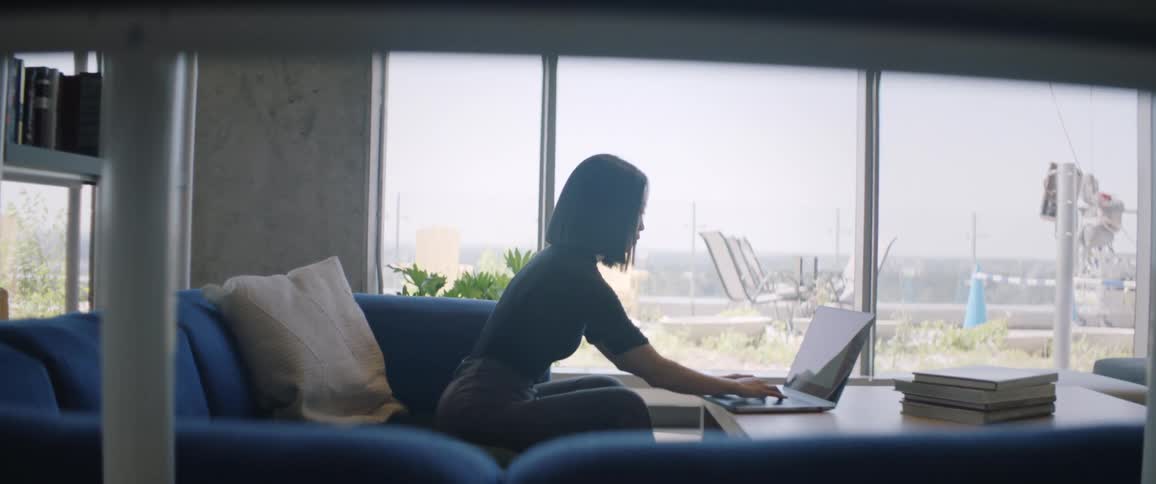 A woman sits on the couch typing on her laptop