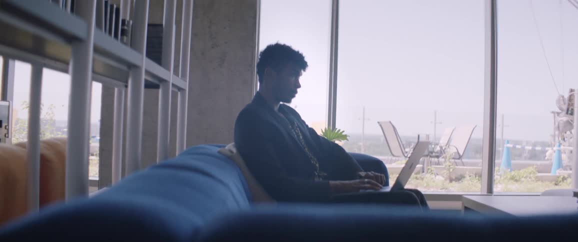 A man is sitting on the couch typing on his laptop