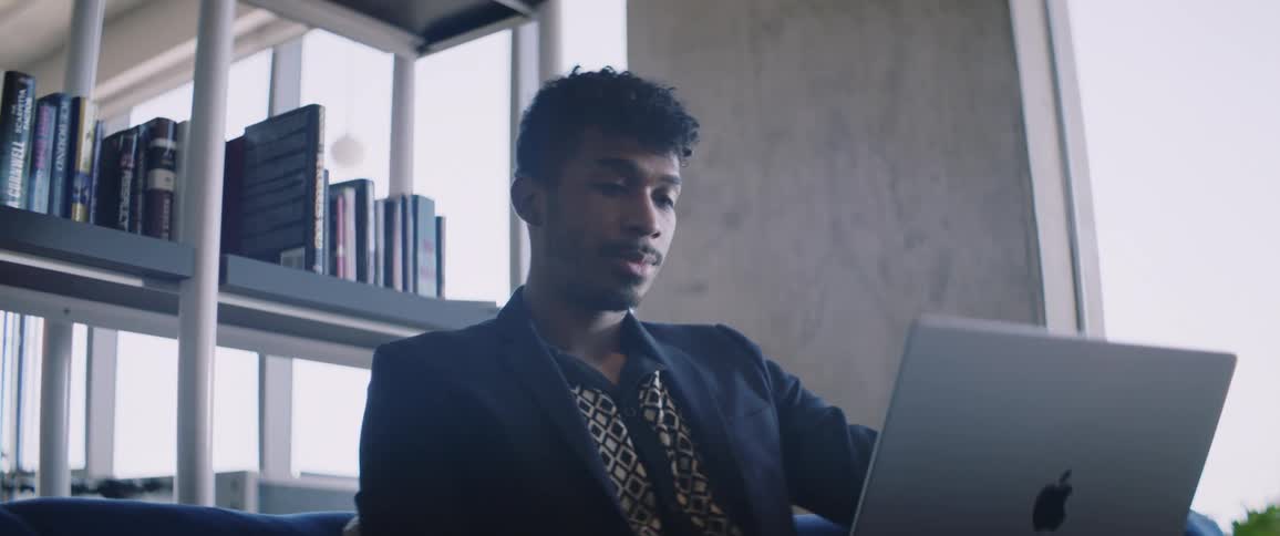 Man sitting in front of a laptop with books on a shelf in the background