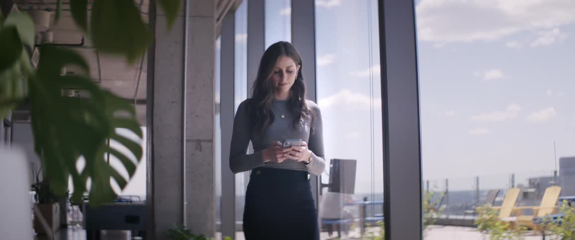 A woman stands inside a spacious office area while looking at her smart phone