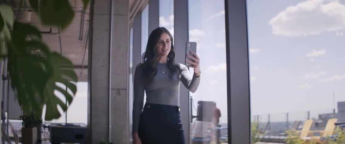 Woman standing in front of a window holding a cell phone in front of her face