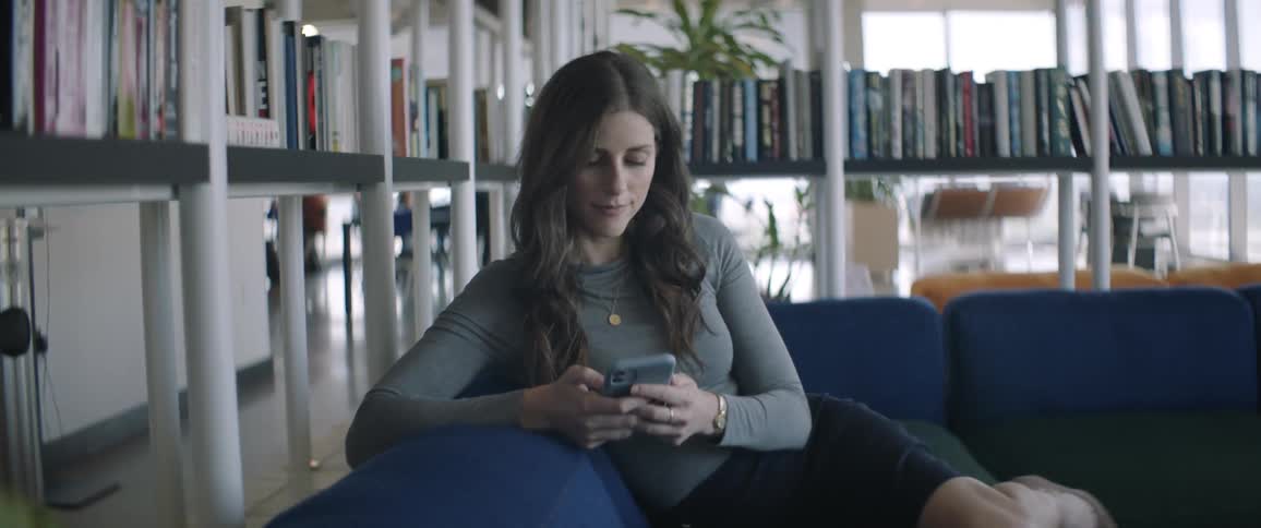 Woman on a blue couch using her cell phone in an indoor work space