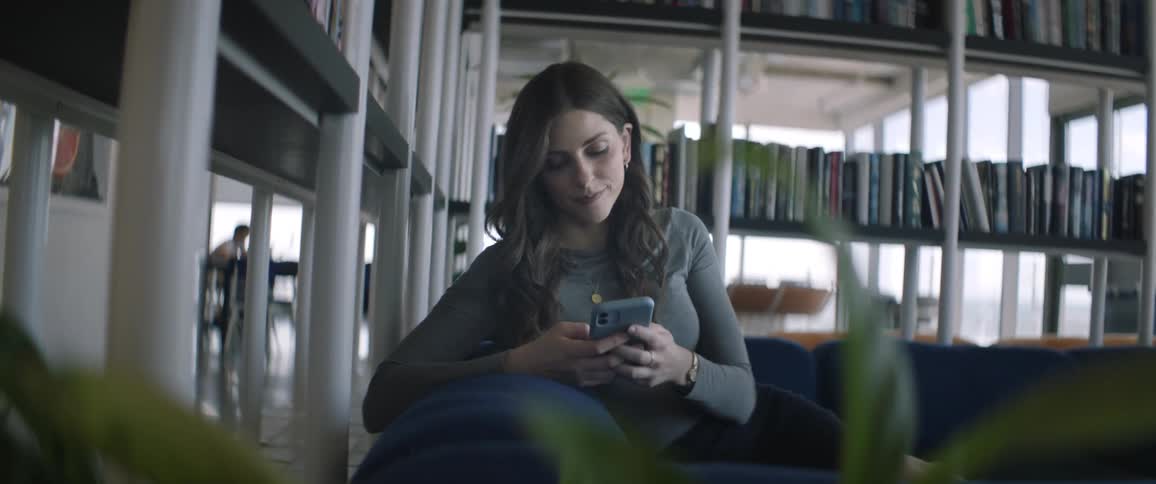 A young woman is sitting on a blue sofa while typing on a cell phone