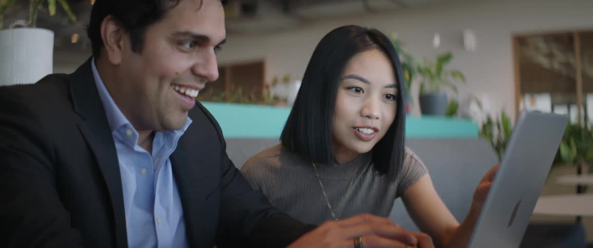 One man and a woman are talking while looking at each other on a laptop and are happy