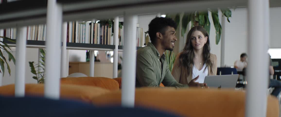 Smiling man and woman sitting side by side on the couch talking and with a laptop