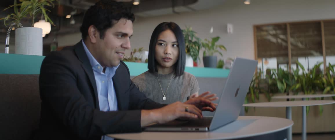 Man and woman sitting side by side at a table while one of them is typing on a laptop