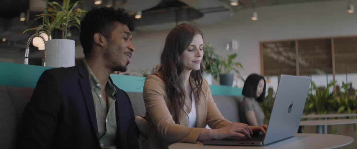 Woman types on laptop and coworker looking at her screen smiles