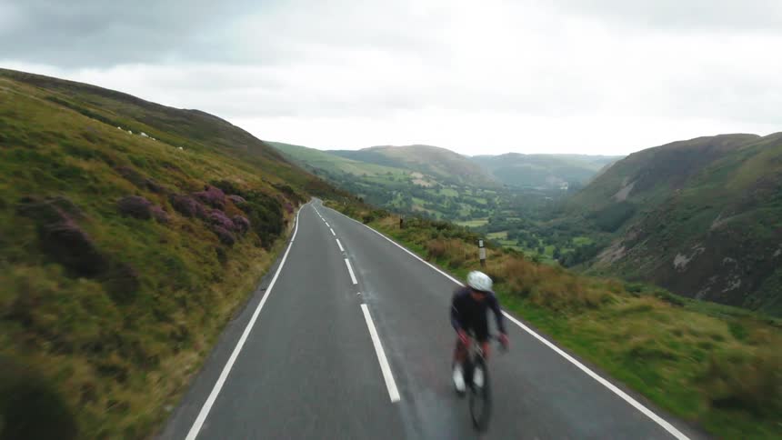Drone passes a female cyclist on a mountain road
