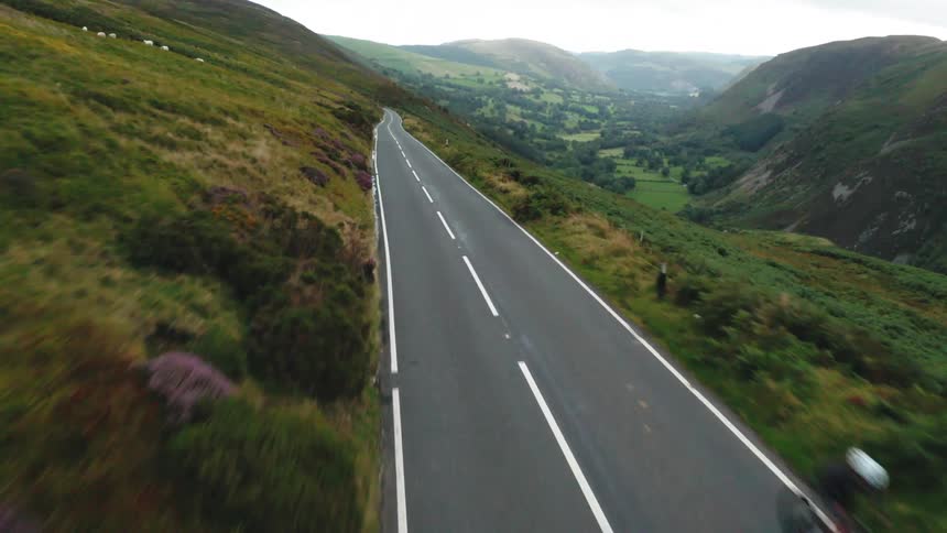 Female cyclist races up hill road surrounded by mountains