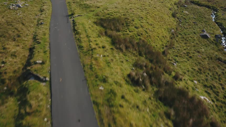 Woman cycles hard up hill on remote road surrounded by lakes and mountains