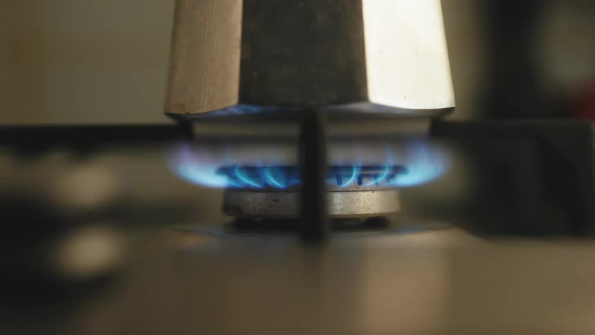 Closeup of a stove burner lighting a fire and heating a metal kettle