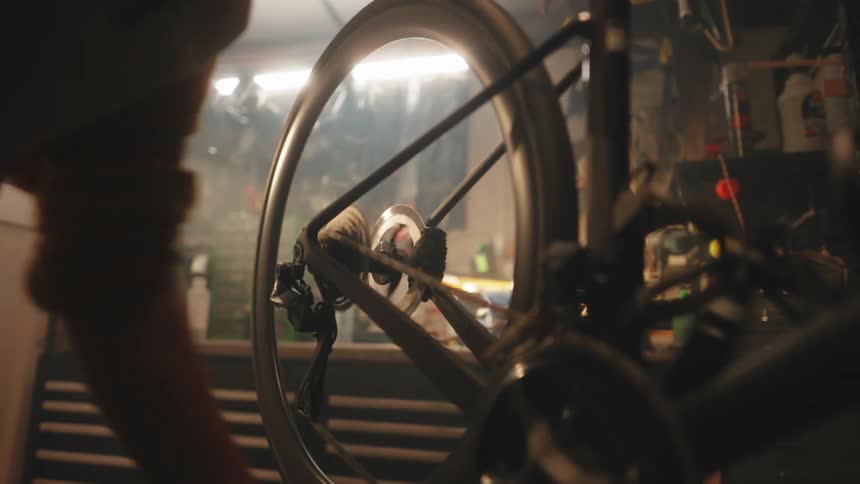 Hand of a woman turning the crank of a bicycle inside a workshop