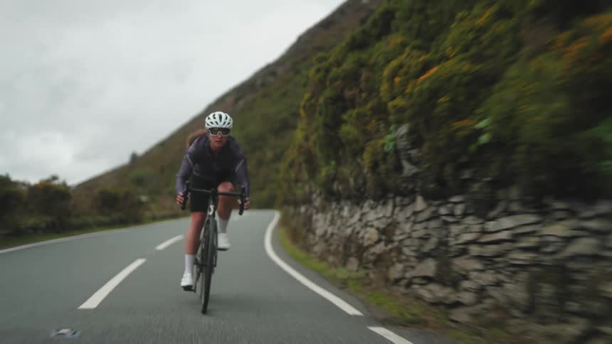 Woman cycles fast down a hill with mountains