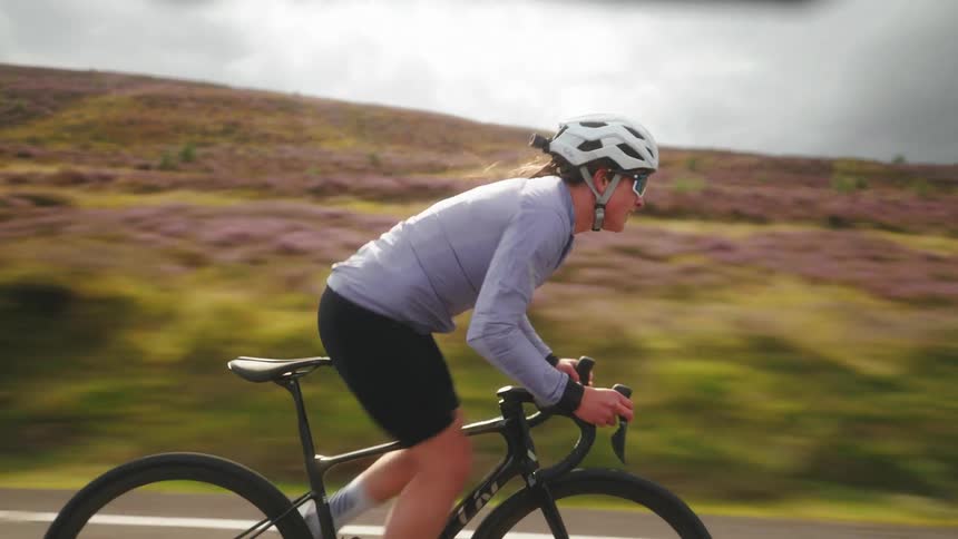 Dynamic female cyclist pedals along fast road on an overcast day