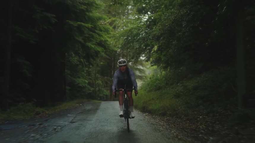Cyclist woman cycling along forest road free wheeling on road bike