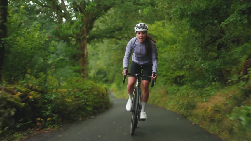 Woman cycling fast along road in forest smiling and happy