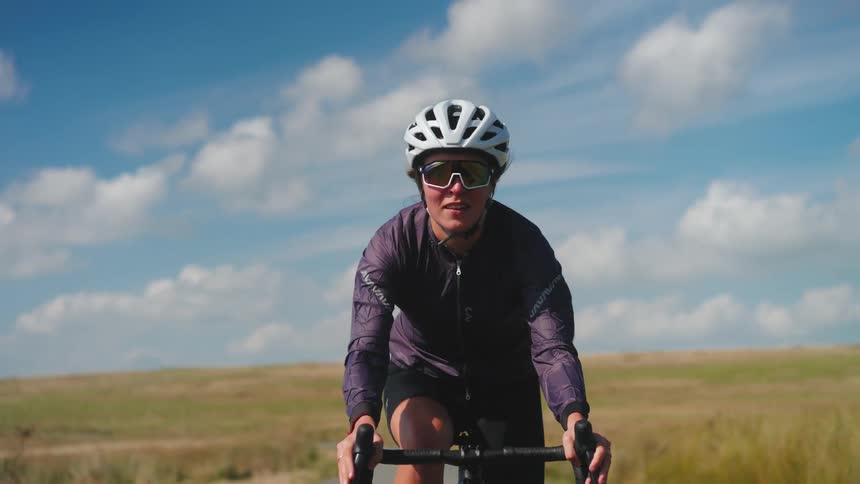 A woman cycles down a bicycle trail through grass lands