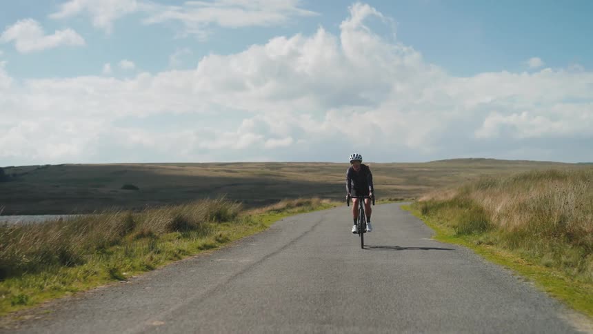 A female cyclist on a narrow street by a lake with mountains around