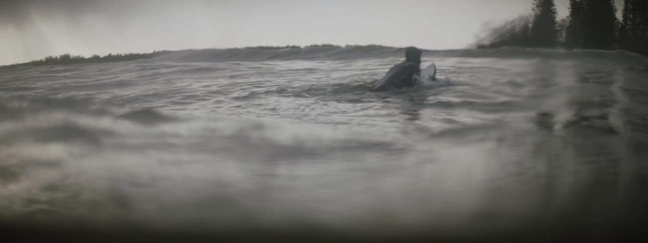 A surfer gets up on his surfboard as a wave moves toward him
