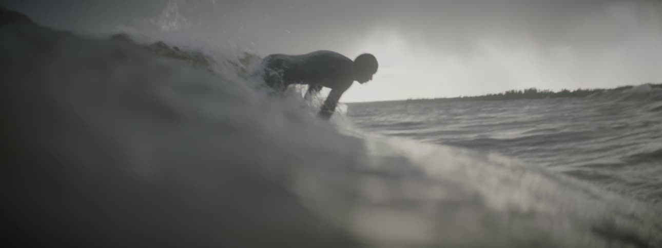 A surfer stands up and rides a wave while another paddles through it