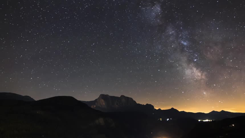 Stunning night landscape with the milky way stretching over mountains and city lights in the distance