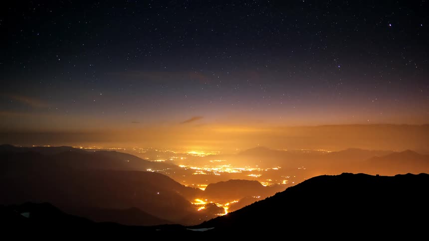 Silhouette of mountains and a dawn starry sky with an illuminated city on the horizon