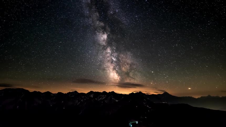 Night view with the milky way shining above dark mountains and distant lights