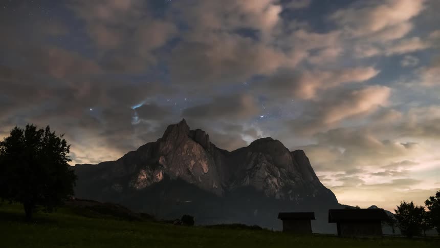 Night landscape with mountains in the background under a partly cloudy and starry sky